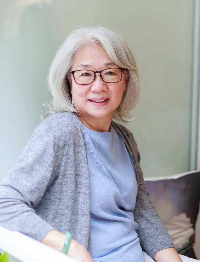 Photo of a senior woman with glasses at home sitting on the couch and smiling.