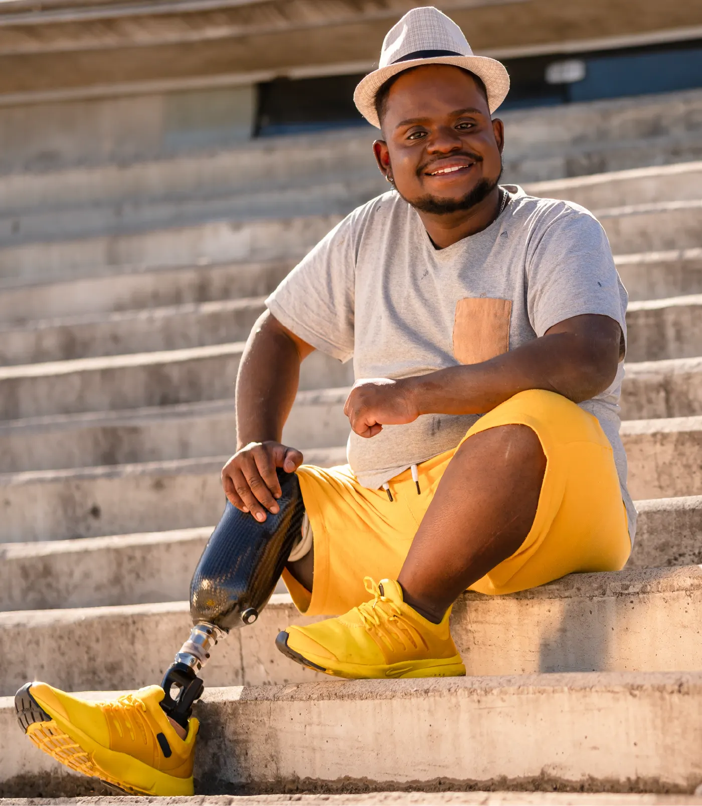 Photo of a man sitting on a the steps to a building with a hat on and smiling.